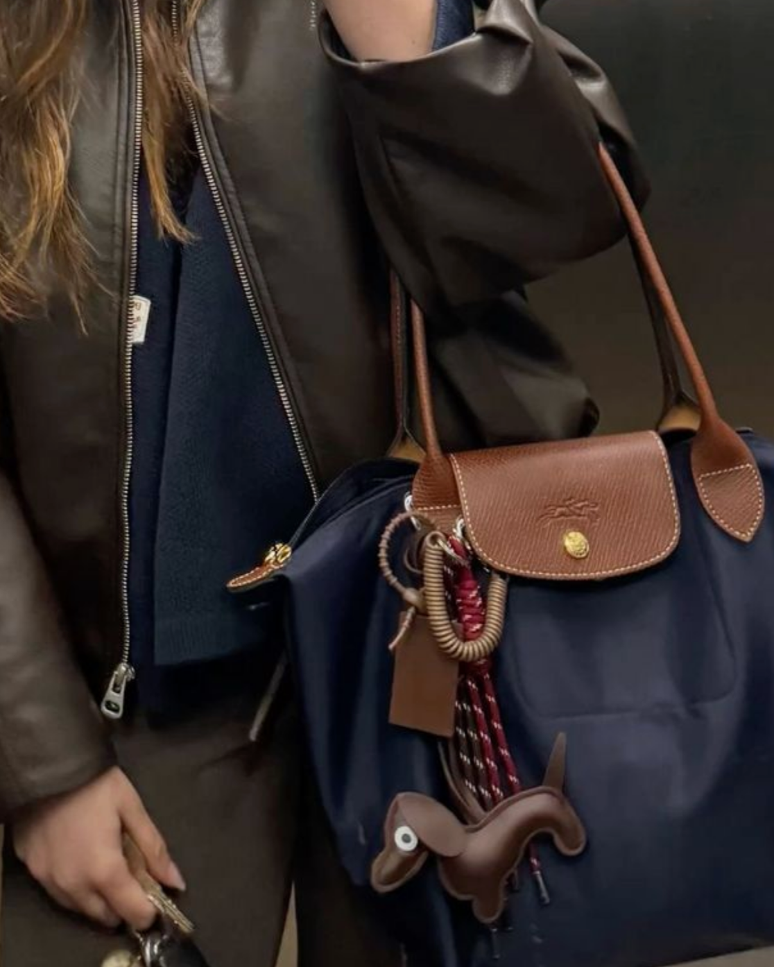 Person holding a blue bag with a brown leather tag and decorative charm.