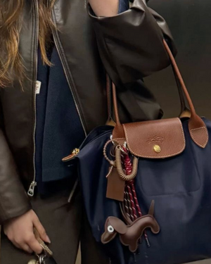 Person holding a blue bag with a brown leather tag and decorative charm.