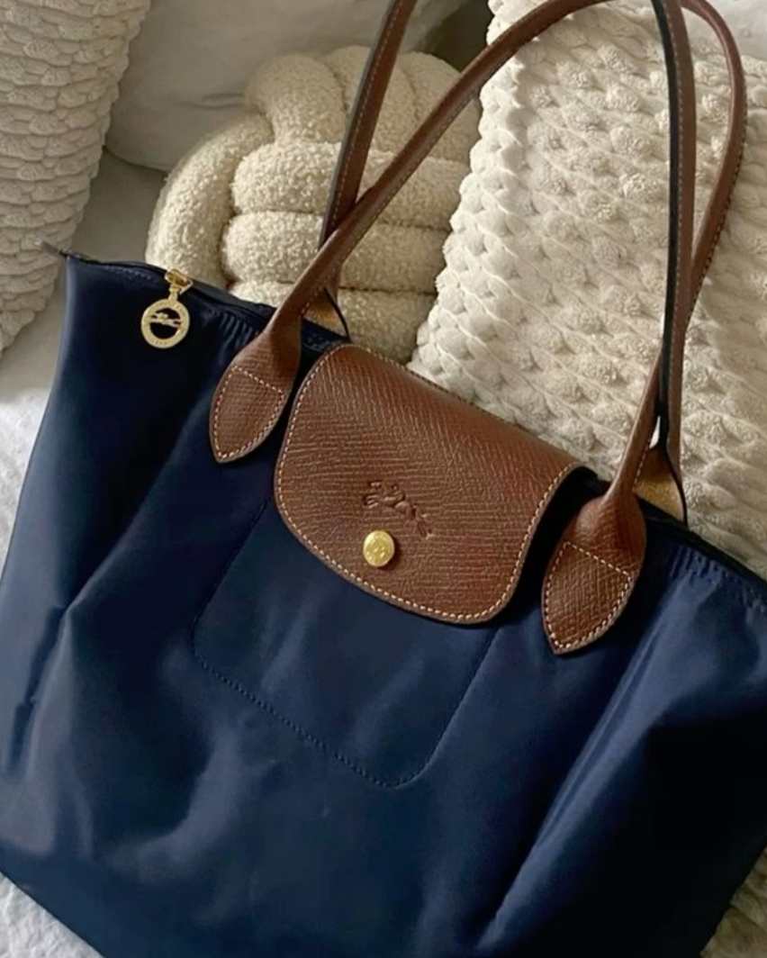 Navy blue handbag with brown leather handle and flap on a textured white surface