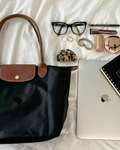 Black handbag with accessories including glasses, makeup items, and a laptop on a white surface.