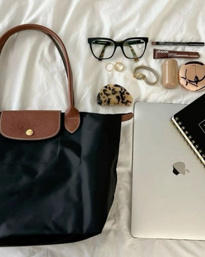 Black handbag with accessories including glasses, makeup items, and a laptop on a white surface.
