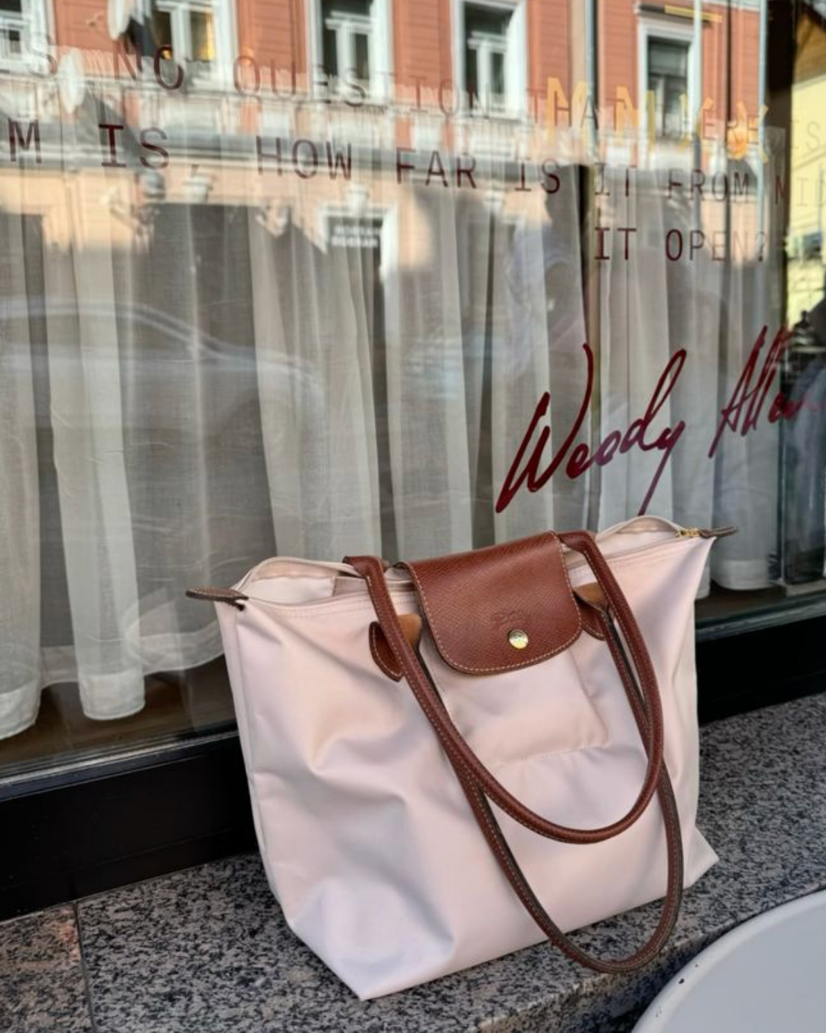White tote bag with brown handle on a window sill with 'Woody Allen' branding.